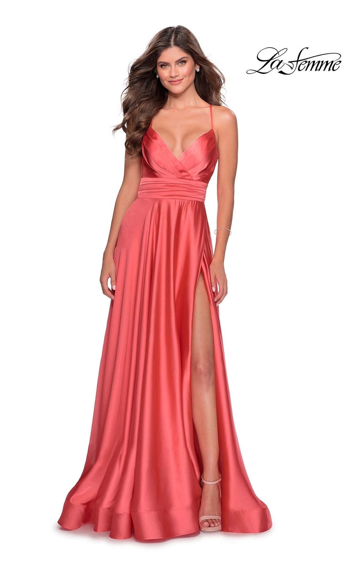 A woman smiles in the La Femme Banded-Waist Long A-Line Prom Dress 28571, a sleeveless coral satin gown with a high slit, fitted bodice, and flowing skirt. The